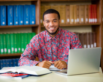 man smiling at desk with laptop and book