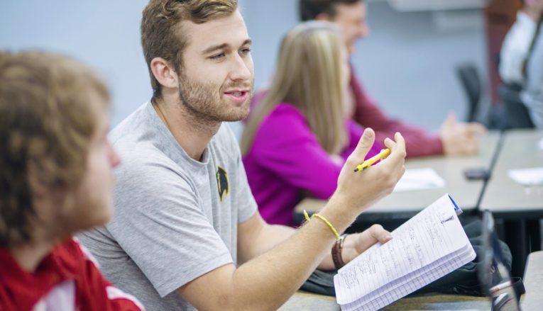 Student holding notebook and talking in class